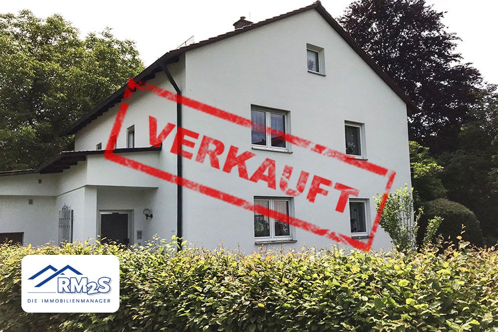 Weißes Wohnhaus mit Satteldach hinter einer Hecke